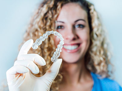 A woman is holding a transparent dental retainer in her hand.